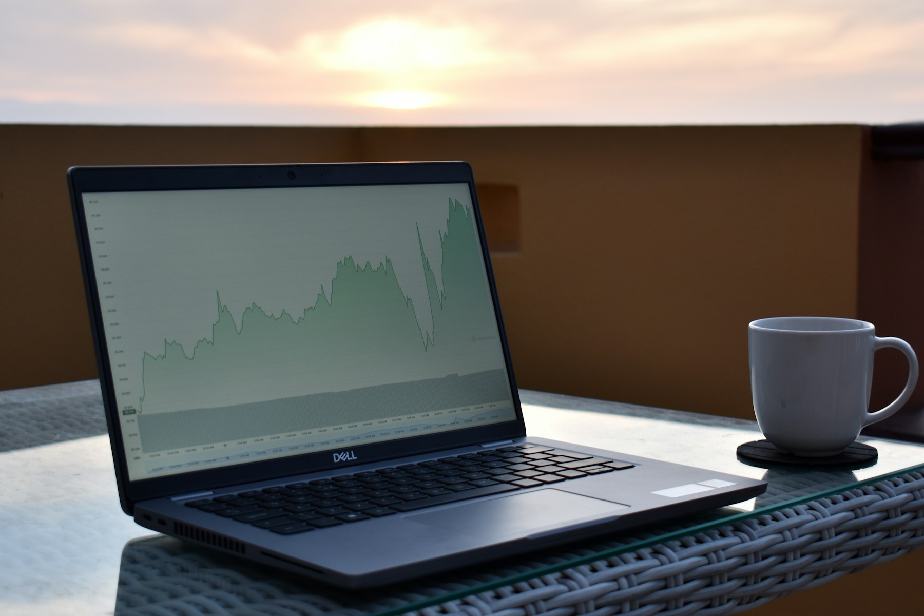 Laptop with a financial chart and a cup of coffee on a balcony at sunrise